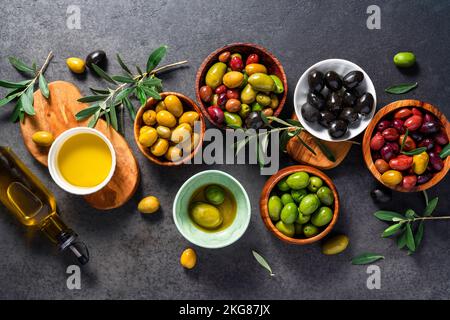 Verschiedene Oliven in der Schüssel auf dunklem Hintergrund. Oliven und eine Flasche Oliven. Draufsicht. Diät-Food-Konzept. Leckere Oliven. Stockfoto