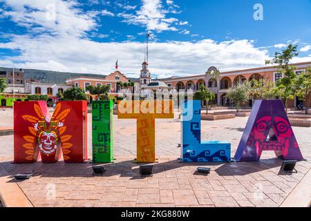 Ein farbenfrohes Schild auf dem Stadtplatz für San Pablo Villa de Mitla, Oaxaca, Mexiko. Dahinter befindet sich das Rathaus oder der Stadtpalast mit dem Uhrenturm. Stockfoto