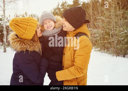 Mama und Papa kuscheln und küssen ihren kleinen Sohn im Winterpark. Stockfoto