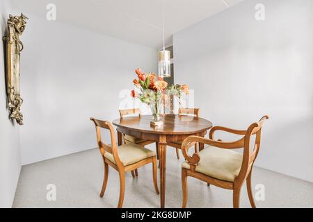 Tisch mit Stühlen und Blumen unter glühenden Lampen gegen platziert Küche und Tür in zeitgenössischem Haus Stockfoto