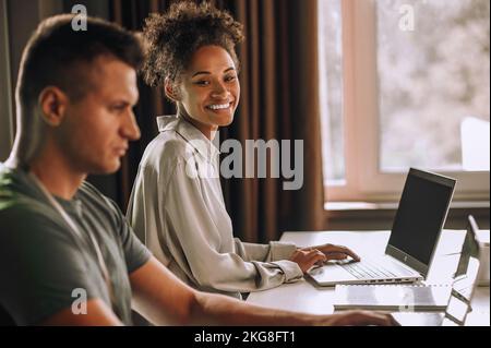 Freudige Mitarbeiterin und ihre Kollegin, die an Laptops arbeiten Stockfoto