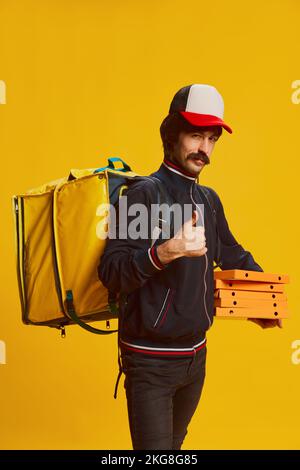 Porträt eines Liefermannes mit Schnurrbart und Pizzaschachteln isoliert auf gelbem Hintergrund. Lebensmittellieferungsgeschäft Stockfoto