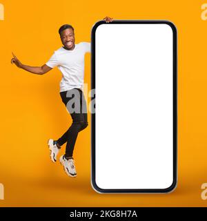 Onlinewerbung. Joyful Black Guy Springt In Der Nähe Des Riesigen Leeren Mobiltelefons Stockfoto