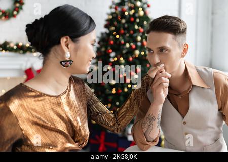 Tätowierte Mann küsst Hand von lächelnden asiatischen Frau in elegant glänzende Bluse Stockfoto