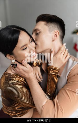 Junger Mann küsst und umarmt glücklich asiatische Frau in elegante Bluse Stockfoto