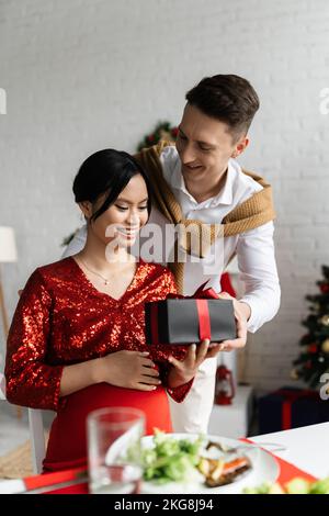 Junger Mann schenkt der schwanger und eleganten asiatischen Frau Weihnachtsgeschenk Stockfoto