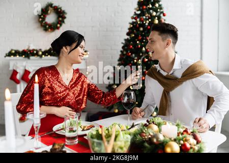Schwanger und fröhlich asiatische Frau Fütterung Mann, während mit Spaß an romantischen Weihnachtsessen Stockfoto