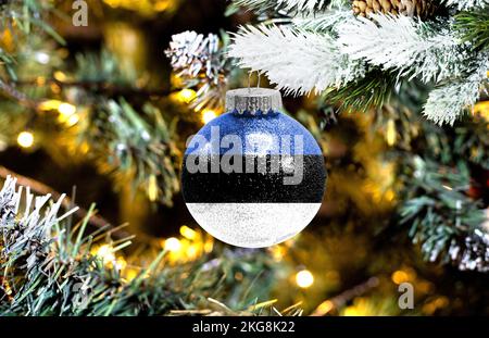 Neujahrs-Glaskugel mit der Flagge Estlands vor einem bunten Weihnachtshintergrund Stockfoto