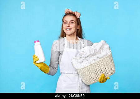 Frau in Gummihandschuhen mit Wäschekorb und Waschmittelflasche Stockfoto