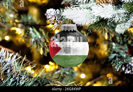 Neujahrs-Glaskugel mit der Flagge Palästinas vor einem bunten Weihnachtshintergrund Stockfoto