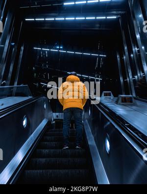 Ein Foto eines Mannes in einem gelben Mantel auf einer Rolltreppe an der Tottenham Court Road Station, London, England. Stockfoto