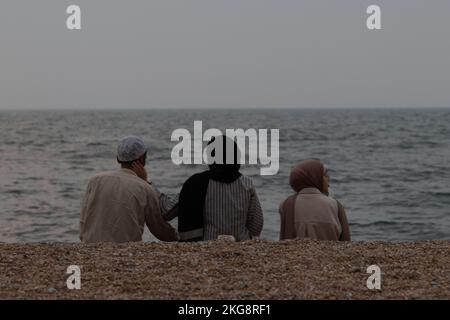 Eine Familie saß an einem steinernen Kieselstrand unter einem grauen Himmel Stockfoto