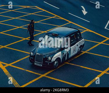 Ein Mann, der die Straße überquert, während ein Taxi in London vor ihm abbiegt, an einer Kreuzung bei Kings Cross in London Stockfoto