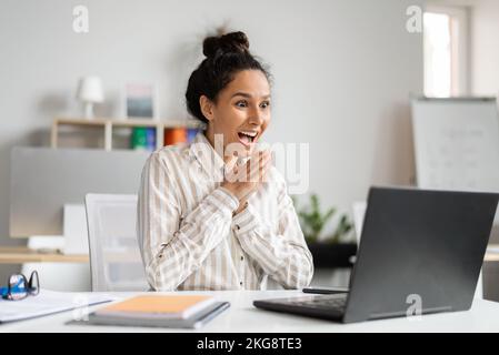 Beförderung, Gewinnkonzept. Aufgeregte Geschäftsfrau, die großartige Neuigkeiten und Glück feiert und sich vor Freude auf den Laptop-Bildschirm blickt Stockfoto