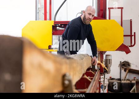 Junger Mann, der an der Maschine für die Holzverarbeitung arbeitet, großer Holzschneider oder Säge, Industriekonzept Stockfoto