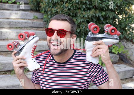 Mann mit 1980er-Look, der Rollschuhe hält Stockfoto