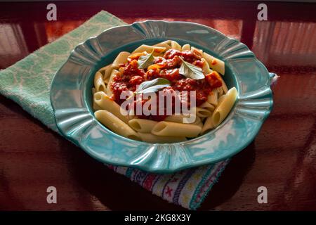 Goiânia, Goias, Brasilien – 22. November 2022: Hellgrüner Teller mit einer Portion Pasta (Penne) mit Tomatensoße und Basilikumblättern. Stockfoto