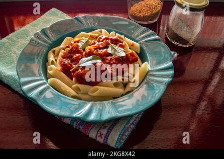 Goiânia, Goias, Brasilien – 22. November 2022: Hellgrüner Teller mit einer Portion Pasta (Penne) mit Tomatensoße und Basilikumblättern. Stockfoto