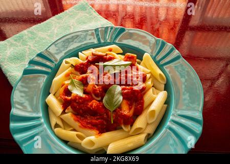 Goiânia, Goias, Brasilien – 22. November 2022: Hellgrüner Teller mit einer Portion Pasta (Penne) mit Tomatensoße und Basilikumblättern. Stockfoto