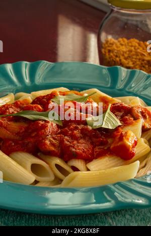 Goiânia, Goias, Brasilien – 22. November 2022: Detail einer hellgrünen Platte mit einer Portion Pasta (Penne) mit Tomatensoße und Basilikumblättern. Stockfoto