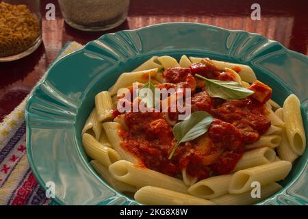 Goiânia, Goias, Brasilien – 22. November 2022: Hellgrüner Teller mit einer Portion Pasta (Penne) mit Tomatensoße und Basilikumblättern. Stockfoto