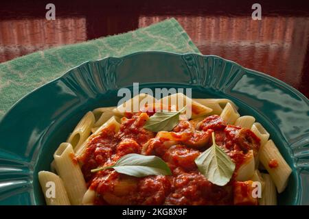 Goiânia, Goias, Brasilien – 22. November 2022: Nahaufnahme auf einem hellgrünen Teller mit einer Portion Pasta (Penne) mit Tomatensoße und Basilikumblättern. Stockfoto