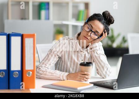 Müde Angestellte, die auf der Arbeit schlafen, erschöpfte Frau, die am Schreibtisch neben einem Laptop und Ordnern ruht Stockfoto