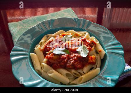 Goiânia, Goias, Brasilien – 22. November 2022: Hellgrüner Teller mit einer Portion Pasta (Penne) mit Tomatensoße und Basilikumblättern. Stockfoto