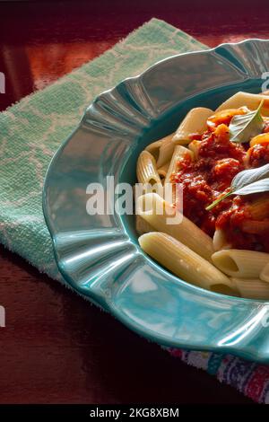 Goiânia, Goias, Brasilien – 22. November 2022: Detail einer hellgrünen Platte mit einer Portion Pasta (Penne) mit Tomatensoße und Basilikumblättern. Stockfoto