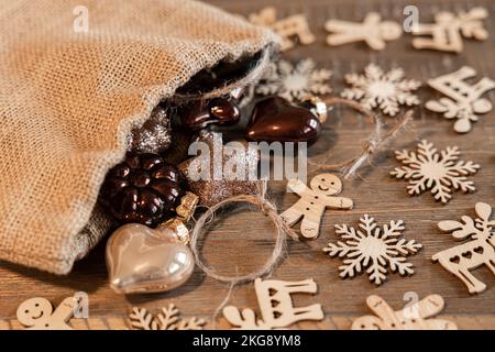 Auf einem alten Holztisch liegt eine Segeltasche mit Weihnachtsbaumschmuck aus Glas und Weihnachtsdekorationen aus Holz Stockfoto