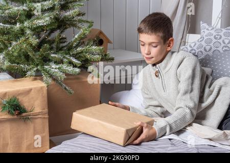 Ein süßer Teenager im Pullover zieht Geschenke unter einem Weihnachtsbaum aus. Silvester-Morgen. Weihnachtsgeschenke Für Die Ganze Familie. Stockfoto