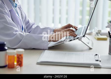 Zugeschnittenes Bild eines leitenden Arztes, der am Schreibtisch in der Arztpraxis am Laptop arbeitet Stockfoto