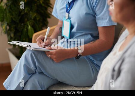 Zugeschnittenes Bild eines Arztes zum Ausfüllen des Dokuments bei einem Besuch des Patienten zu Hause Stockfoto
