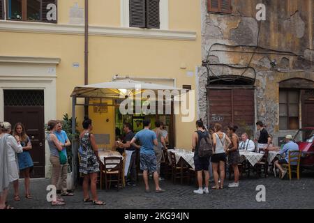 Menschen außerhalb von Da Enzo Al 29, einem beliebten lokalen Restaurant an einer Kopfsteinpflasterstraße im charmanten Trastevere. Touristen warten in der Schlange, während die Einheimischen essen. Stockfoto