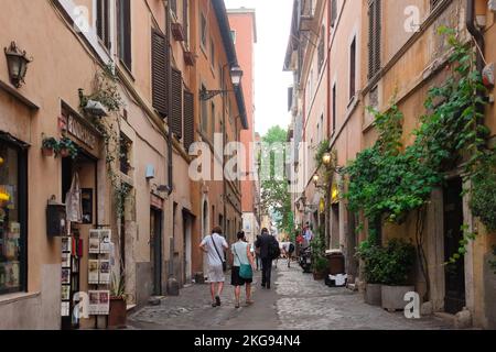 Rom, Italien: Die Leute gehen entlang der Via della Lungaretta, einer malerischen kopfsteingepflasterten Straße mit alten Gebäuden und malerischen Geschäften im charmanten Trastevere Stockfoto