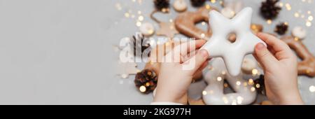 Die Hände der Kinder halten einen Lebkuchen in Sternform. Das Konzept von Weihnachtsbonbons, Spielzeug, Girlanden und Bokeh. Einrichtung für Neujahrsferien. Stockfoto