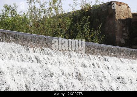 An einem sonnigen Tag fließt frisches Wasser durch Stufen aus Ziegelstein auf einem Staudamm Stockfoto