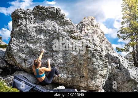Beschreibung: Sportliche Frau klettert nachmittags auf einen Felsblock. Falzarego Pass, Dolomiten, Südtirol, Italien, Europa. Stockfoto