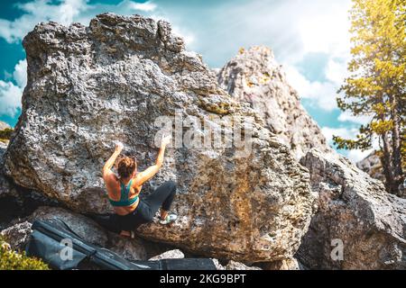 Beschreibung: Sportliche Frau klettert nachmittags auf einen Felsblock. Falzarego Pass, Dolomiten, Südtirol, Italien, Europa. Stockfoto