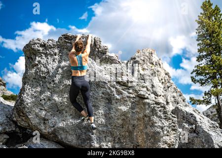 Beschreibung: Sportliche Frau klettert nachmittags auf einen Felsblock. Falzarego Pass, Dolomiten, Südtirol, Italien, Europa. Stockfoto