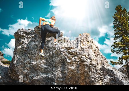 Beschreibung: Sportliche Frau klettert nachmittags auf einen Felsblock. Falzarego Pass, Dolomiten, Südtirol, Italien, Europa. Stockfoto