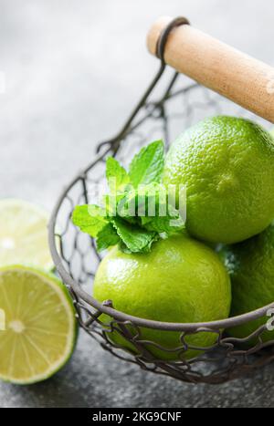 Grüne Limes mit frischen Minzblättern im Korb, betonierter Hintergrund Stockfoto