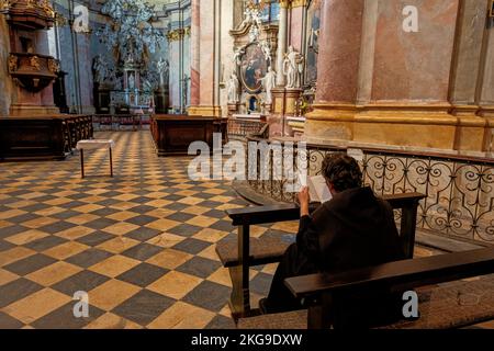 Rajhrad, Tschechische Republik - 22. Mai 2022: Benediktinermönch sitzt in der Kirche St. Peter und Paul und las die Heilige Bibel in Rajhrad, Tschechische Republik. Stockfoto