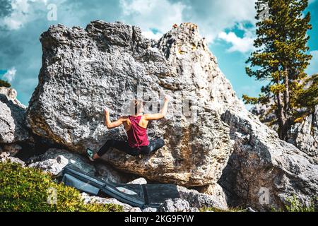Beschreibung: Sportliche Frau klettert nachmittags auf einen Felsblock. Falzarego Pass, Dolomiten, Südtirol, Italien, Europa. Stockfoto
