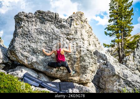 Beschreibung: Sportliche Frau klettert nachmittags auf einen Felsblock. Falzarego Pass, Dolomiten, Südtirol, Italien, Europa. Stockfoto