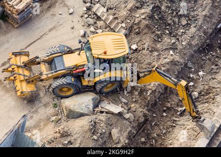 Gelber Traktor mit Schaufel und vor und zurück, der auf einer Baustelle einen Graben aushubt. Blick von oben Stockfoto