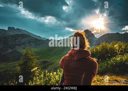 Beschreibung: Sportliche Frau in Outdoor-Jacke sieht sich die wunderschöne Bergkulisse bei Sonnenuntergang an. Falzarego Pass, Dolomiten, Südtirol, Italien, Europa. Stockfoto