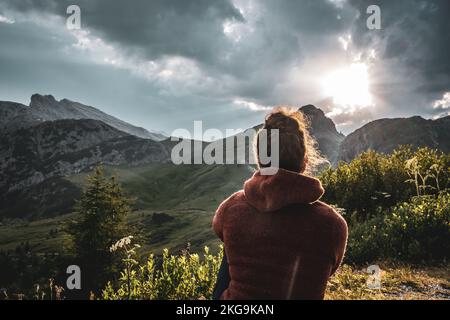 Beschreibung: Sportliche Frau in Outdoor-Jacke sieht sich die wunderschöne Bergkulisse bei Sonnenuntergang an. Falzarego Pass, Dolomiten, Südtirol, Italien, Europa. Stockfoto