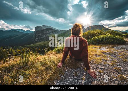 Beschreibung: Sportliche Frau in Outdoor-Jacke sieht sich die wunderschöne Bergkulisse bei Sonnenuntergang an. Falzarego Pass, Dolomiten, Südtirol, Italien, Europa. Stockfoto