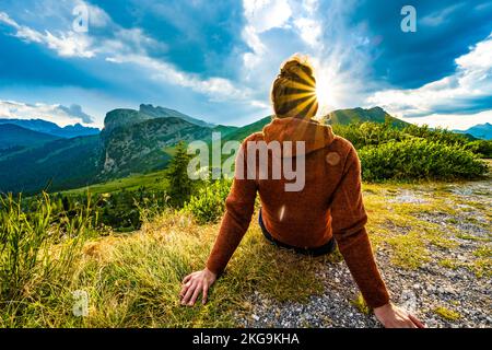 Beschreibung: Sportliche Frau in Outdoor-Jacke sieht sich die wunderschöne Bergkulisse bei Sonnenuntergang an. Falzarego Pass, Dolomiten, Südtirol, Italien, Europa. Stockfoto